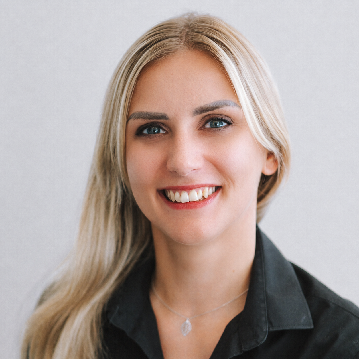 white woman with long blond hair, wears a black collared shirt with a silver necklace.