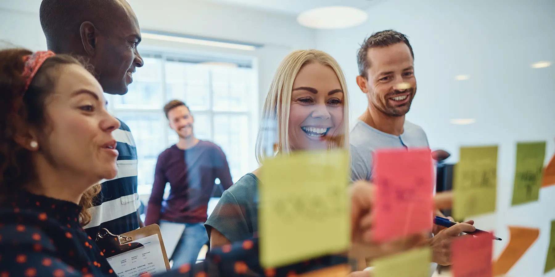 A group of people are placing sticky notes on a piece of glass in front of the camera. They're smiling.