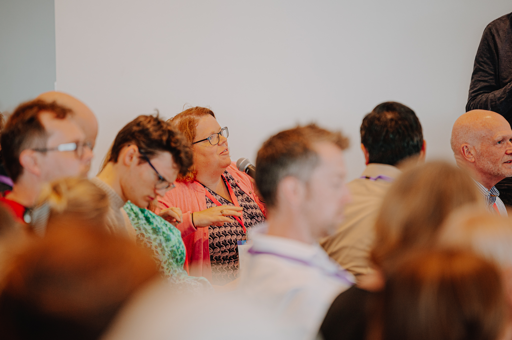 An audience member asks a question using a microphone. She has red long hair, wears a black and white stripy top under an orange cardigan