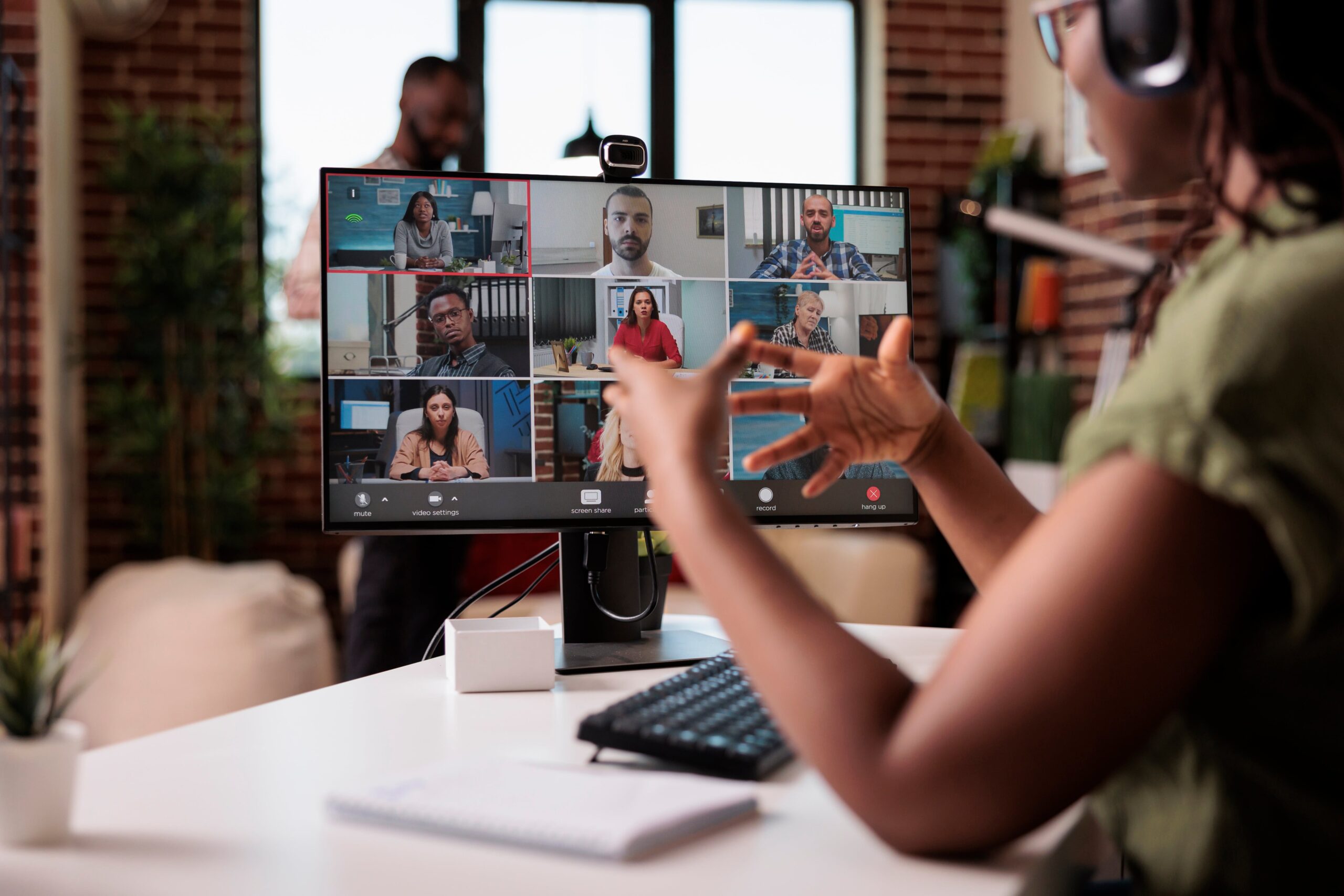 African American startup employee working from home gesturing to colleagues on a conference call at desk.